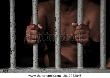 Inmate Hands Behind Bars Representing Incarceration, Black Background
