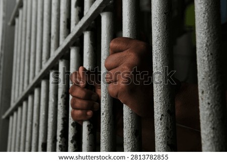 Inmate Hands Behind Bars Representing Incarceration, Black Background