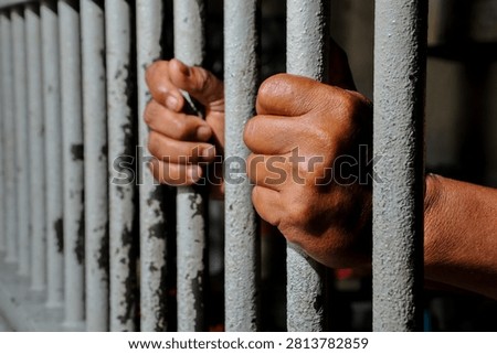 Inmate Hands Behind Bars Representing Incarceration, Black Background
