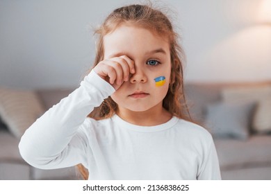 Innocent Child Is Crying. Portrait Of Little Girl With Ukrainian Flag Make Up On The Face.