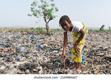 Innocent little African girl who collects recyclable waste in a landfill smiling at the camera not aware of being exploited; child labour concept - Powered by Shutterstock