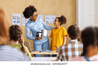 Innovation in education. Student schoolgirl  with virtual reality glasses together with teacher during lesson in bright classroom at school