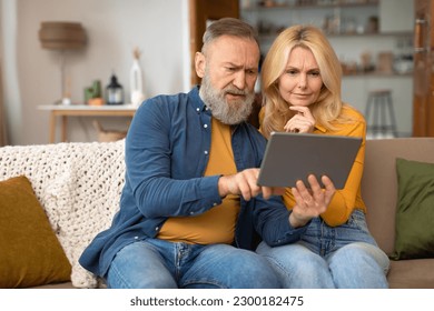 Innovation Touch. Puzzled Senior Couple Using Digital Tablet Having A Hard Time Learning And Browsing Internet Sitting At Home. Seniors Exploring Possibilities Of Online Technology And Gadgets - Powered by Shutterstock