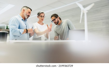 Innovative designers working with 3D wind turbine models in a modern office. Group of creative businesspeople having a discussion while working on a renewable energy project. - Powered by Shutterstock