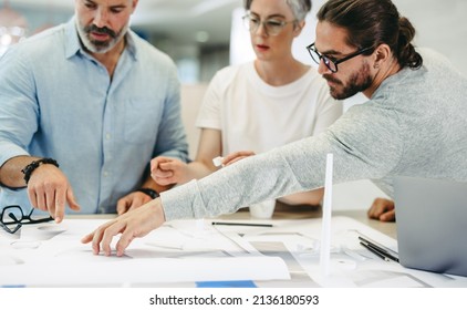 Innovative designers working with wind turbine blueprints in a modern office. Group of creative businesspeople having a discussion while working on a renewable energy project. - Powered by Shutterstock