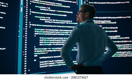 Innovative Startup Concept: Thoughtful Software Engineer Finding Solution, Planning Strategy, Standing and Doing Data Analysis on Big Wall Screen. Programmer Developing e-Commerce App. Back View Shot