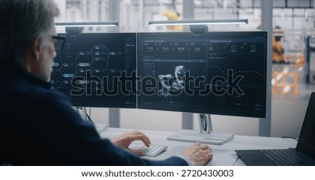 Innovative Workplace, Engineer Using Advanced Software For Robotics. Man Using Advanced Software Manage Robotics, Seated Innovative Dual Screen Workstation. Highlights RD and Technological Innovation.
