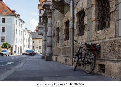 Innsbruck, Austria - April 17, 2019: Black Bicycle With Bicycle Basket On The Sidewalk Next To A Busy Street Leaning Against Brown Stone Wall Of A Building In The City Center Of Innsbruck 