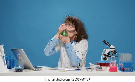 Insane Foolish Female Chemist Using Laptop And Beaker In Front Of Camera, Acting Crazy And Amusing. Mad Funny Woman With Messy Wacky Hair Looking Goofy And Funny, Being Silly In Studio.