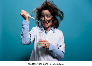 Insane scientist grinning creepy while dripping chemical compounds from pipette into glass flask filled with liquid substance. Mad foolish lab worker using pipet to mix experimental serum. Studio shot