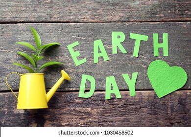 Inscription Earth Day with young plant in watering can on grey wooden table - Shutterstock ID 1030458502