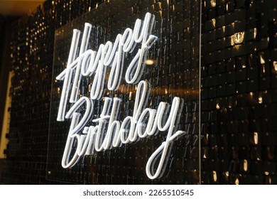 The inscription Happy Birthday is made of LED strip against the background of a wall of sequins. Decoration for the party.