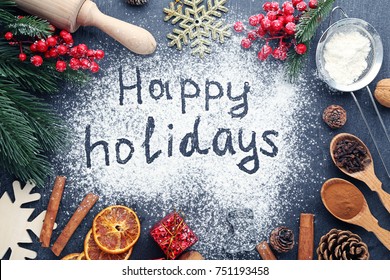 Inscription Happy Holidays on wheat flour background with fir-tree branches, orange fruits and cones