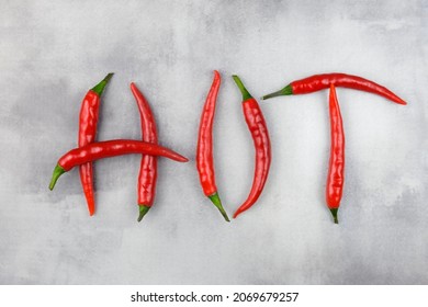 The inscription HOT is laid out from pods of red hot chili peppers on an abstract gray background. Creative image of spices.