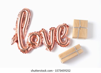 The inscription love in the form of a balloon in pink gold color on a white background. gift boxes of various sizes in craft paper. Flat lay.