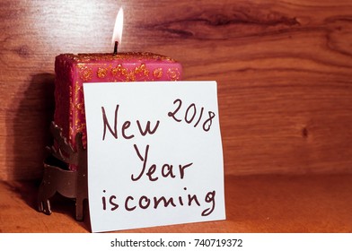 inscription new year 2018 is coming on the background of a candle and a wooden table