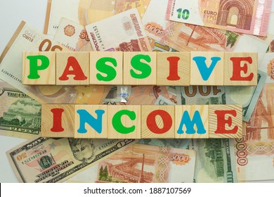 The inscription passive income in multicolored cubes on the background of banknotes euro dollars rubles - Shutterstock ID 1887107569