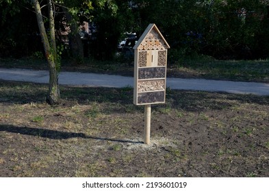 Insect Nest House Located In The Park On The Meadow. It Contains Porous Natural Materials Into Which Insects Can Lay Eggs And Pupae. On The Side Is A Watering Hole For Bees For Water Shape Of Plate