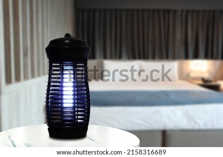 an insects mosquito electric blue light killer lamp is put on the white marble table in the nice bedroom with curtain background to protect the mosquito during sleeping time