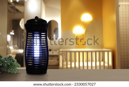 an insects mosquito electric blue light killer lamp is put on the nice wooden table with small plant in yellow children bedroom to protect the mosquito during sleeping time at night