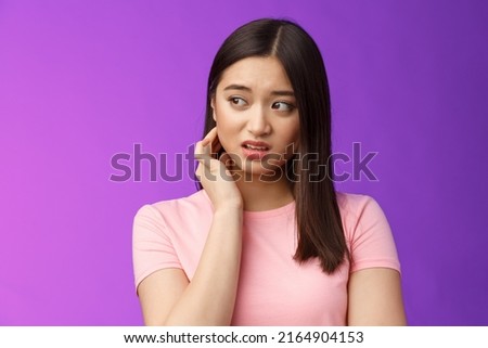 Insecure anxious young timid asian girl feel nervous scared, scratch neck worried, look sideways alarmed, feel danger, standing upset purple background distressed suffer discomfort