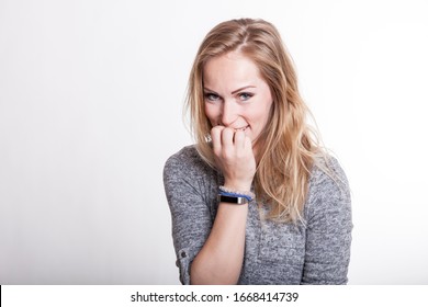 insecure woman chewing her fingernails while planning her irascible revenge. shy blond woman isolated against white background. studio portrait shot.