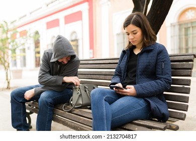 Insecurity Concept. Beautiful Young Woman Sitting On A Bench And Texting On The Smartphone While A Thief Pickpocket Her Wallet 