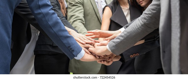Inselective focus of close up side view of people putting their hands together. Businessman friends with stack of hands showing unity and teamwork againt bank and business building center background.