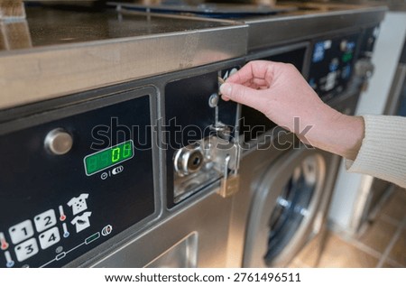 Inserting coin into washing machine in laundromat close up of hand using self service laundry equipment payment concept