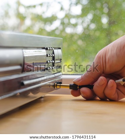Inserting of the headphone cable plug into standard jack of CD player, human hand against window background 