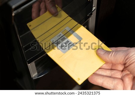 Inserting an old 3 and a half inch floppy disk into a desktop computer.