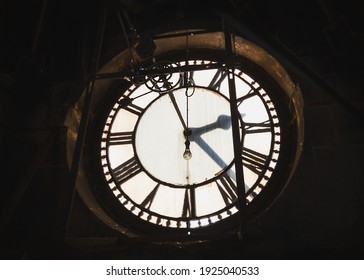 Inside abandoned old ancient clock tower with Roman numerals gears and light bulb hanging down to illuminate from behind hour minute and second hands ticking by - Powered by Shutterstock