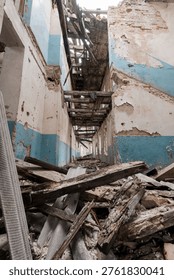 Inside an abandoned structure showcasing crumbling walls, scattered wood debris, faded blue paint, and collapsed ceiling beams highlighting urban decay and neglect
