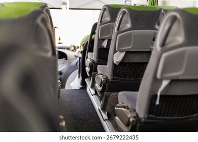 Inside a bus, the scene captures empty, modern seats arranged tidily along the aisle. Bright daylight streams through the large windows, creating an inviting atmosphere.