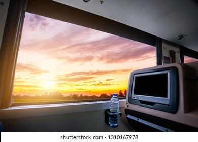 Inside Of The Bus Which Has LCD Screen Blank Rear Seat For Entertainment With A Bottle Of Water And Window View Of Beautiful Landscape Nature With Sky Cloud Sunset, Figure Tourism Road Trip Concept.