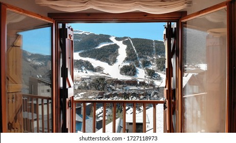Inside of a cabin looking out of the balcony windows at the mountain with the ski slopes filled with snow on a hot winter day with a blue bright sky ready to go skiing