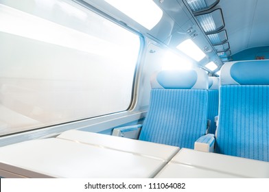 Inside Cabin Of Modern Express Train. Nobody In Blue Chairs At Window. Motion Blur. Comfortable Chairs And Table In Foreground, Sun In Background. Travel, France, Europe.