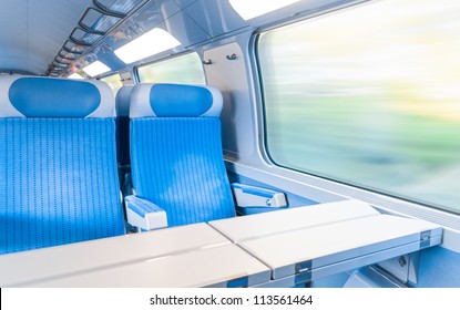 Inside Cabin Of Modern Express Train. Nobody In Blue Chairs At Window. Motion Blur. Comfortable Chairs And Table In Foreground, Nature Outside Window. Travel, France, Europe.