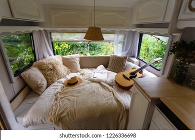 Inside the camper van. Unfilled bed, pillows, guitar, book, hat, white wooden decoration of the house on wheels. - Powered by Shutterstock