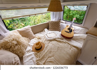 Im Wohnwagen. Ungefülltes Bett, Kissen, Gitarre, Buch, Hut, weiße Holzdekoration des Hauses auf Rädern.