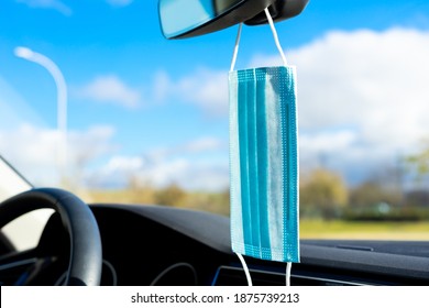 Inside A Car, It Looks Like A Face Mask Is Hanging From The Rearview Mirror. You Can See In The Background That It Is A Beautiful Blue Sky Day