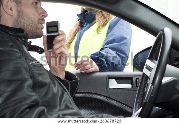 Inside the car view of a young driver subjected\
to breathalyzer test for\
alcohol