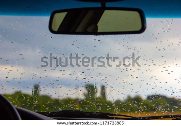 Inside the car with\
water drops on the wind shield glass on an autumn and rainy fall\
day with rear view\
mirror