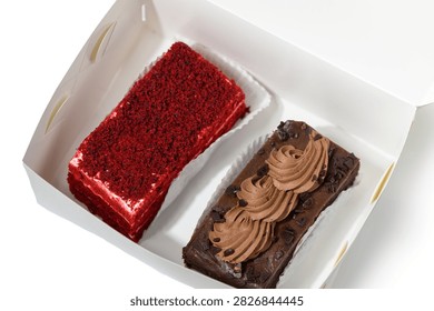 Inside a charming bakery box, two enticing desserts beckon. A slice of velvety red velvet cake stands proudly beside a rich chocolate treat adorned with smooth frosting and chocolate shavings, promising pure bliss.