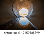 Inside a circular concrete drainage culvert with a trickle of water