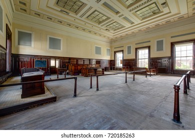 Inside A Derelict Courtroom With Rich Colored Wood Paneling And Pastel Yellow Paint In An Abandoned Courthouse In Massachusetts.