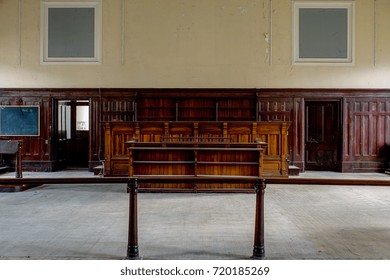 Inside A Derelict Courtroom With Rich Colored Wood Paneling And Pastel Yellow Paint In An Abandoned Courthouse In Massachusetts.