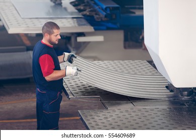 Inside a factory, industrial worker in action on metal press machine holding a piece of steel ready to be worked.