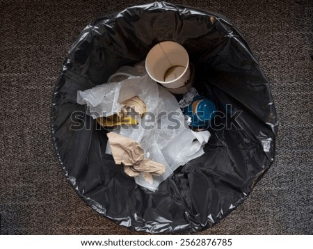 Inside of a garbage or trash can with trash including empty coffee cup, waste paper, banana peel