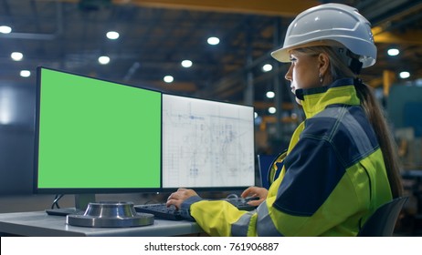 Inside The Heavy Industry Factory Female Industrial Engineer Works On The Personal Computer With Green Mock-up Screen. Secondary Monitor Shows Blueprints.